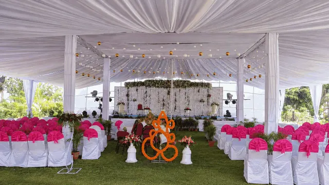 White-draped wedding pavilion with pink-sashed chairs and a marigold Ganesha