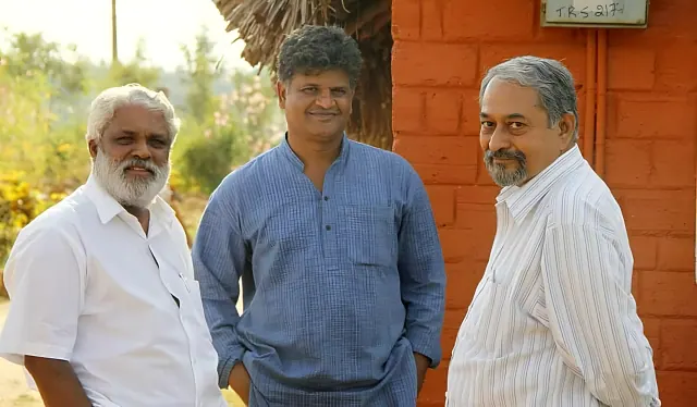 K. B. Siddaiah and K. T. Shivaprasad with founder Prithvi Mallanna beside a brick cottage at Saakshi Retreat