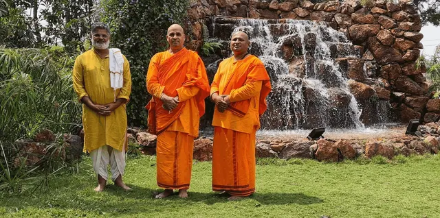 Swami Veereshananda Saraswathi and Swami Paramananda in saffron robes beside the waterfall at Saakshi Retreat