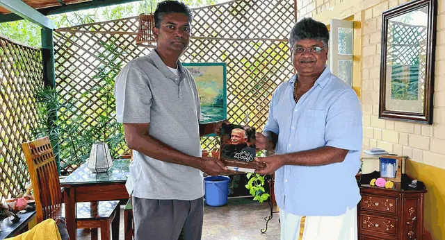 Satish Jarkiholi with founder Prithvi Mallanna, holding a Kannada book, on the verandah at Saakshi Retreat